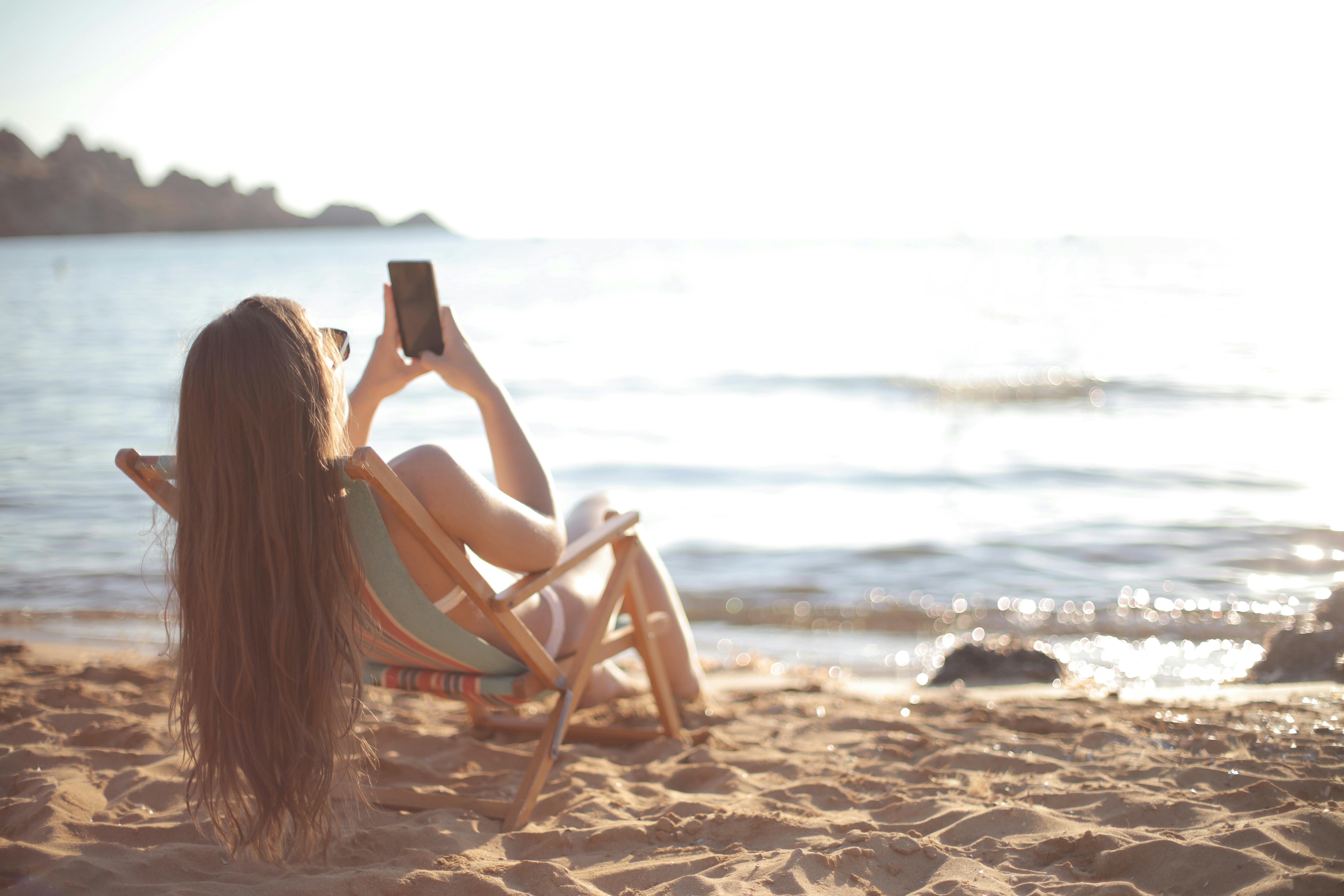 digital detox - una foto di una donna bianca che si rilassa sulla spiaggia guardando il suo telefono