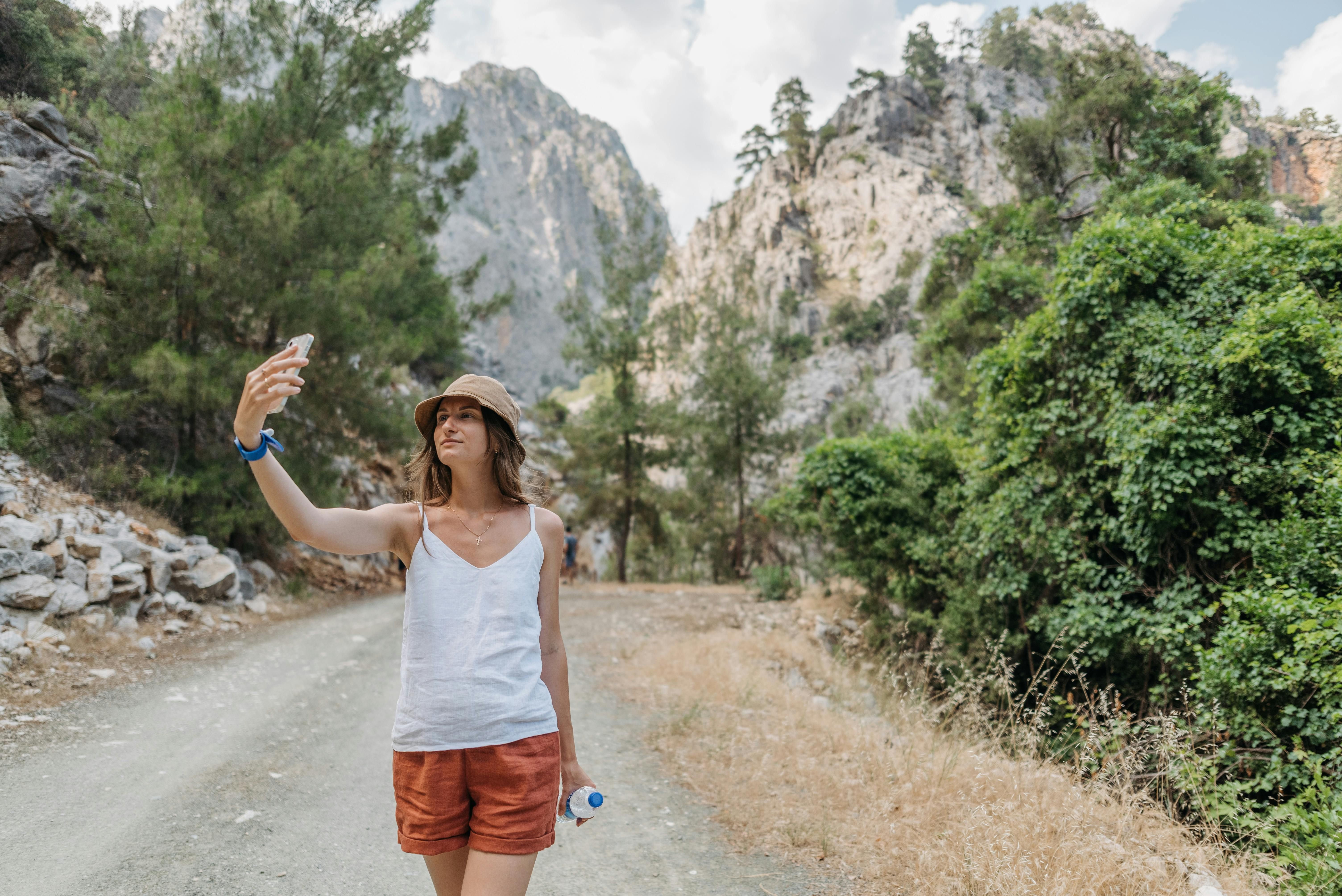plan esim local - photo d'une jeune femme coiffée d'un chapeau à godets marchant sur une route rurale pittoresque en tenant son téléphone 