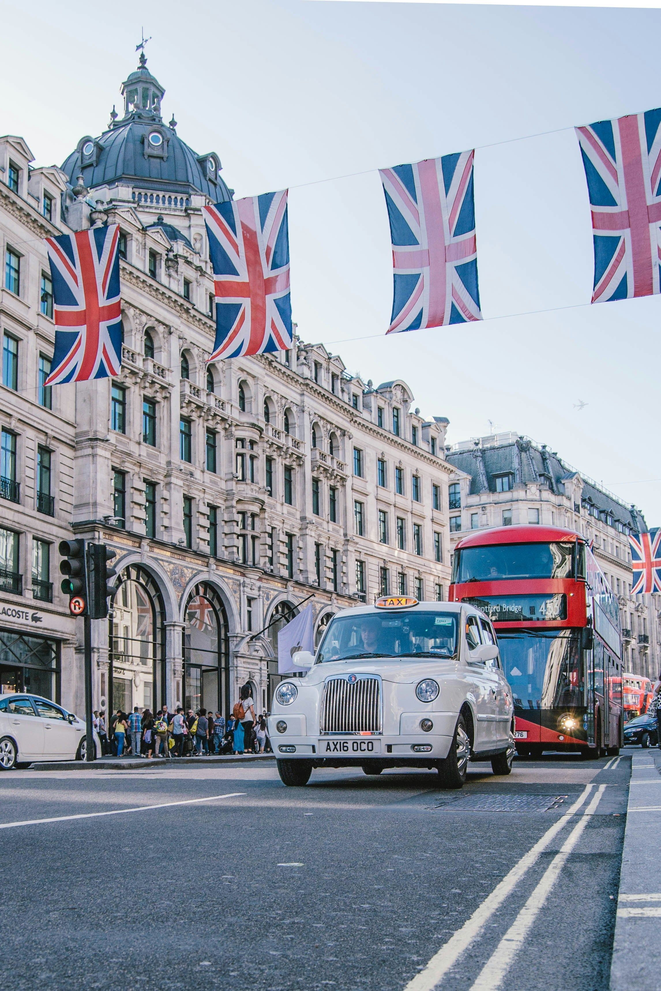 A white car and a red bus driving down a London street.