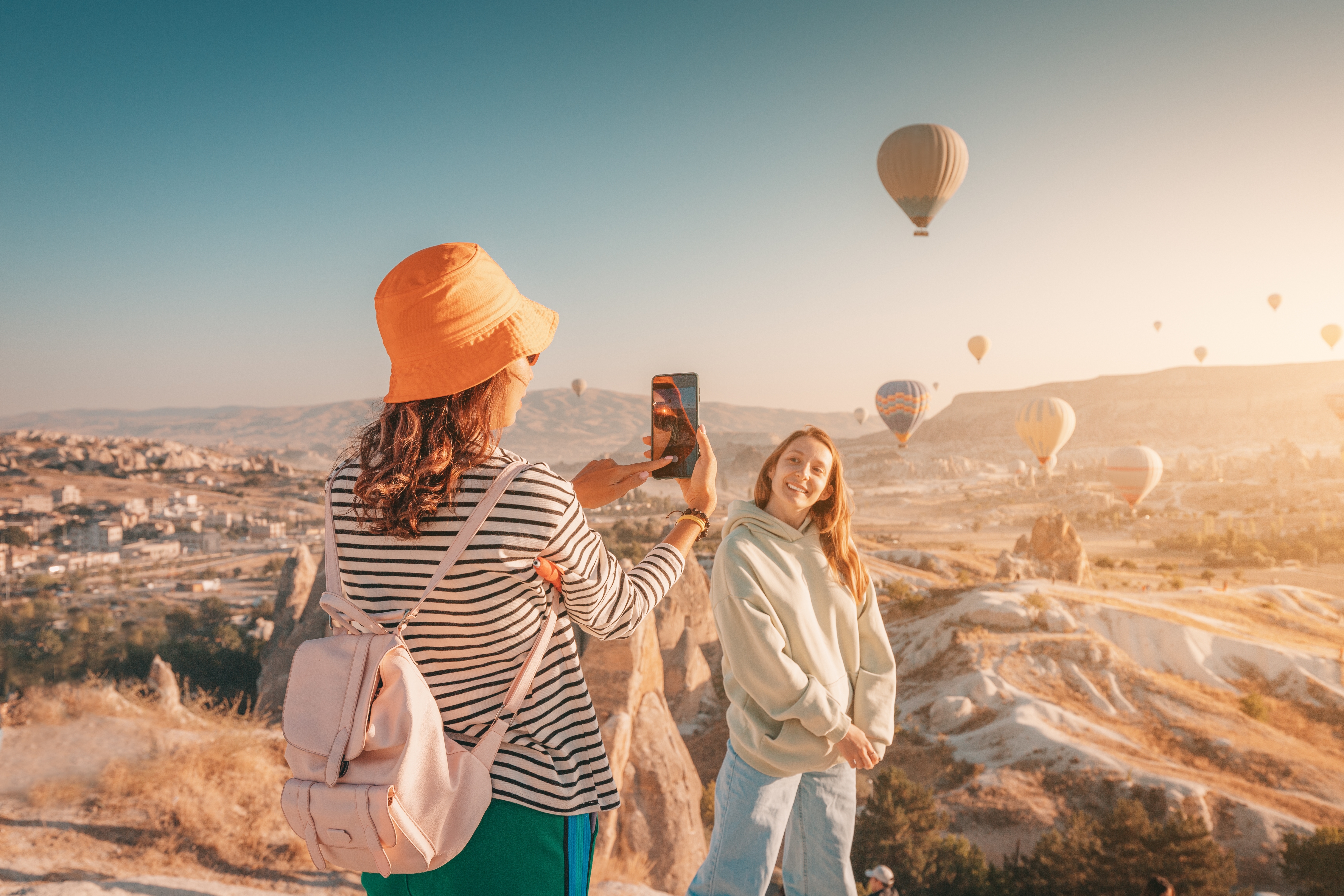 2 giovani donne in Turchia a un festival di mongolfiere che scattano foto con uno smartphone